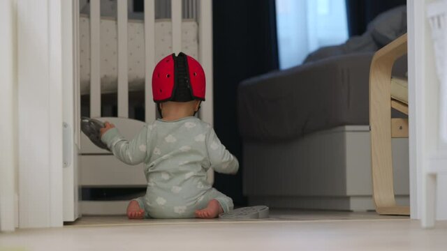 Cute baby boy wearing soft safety helmet discovering new things at home, 7 month old infant on the floor playing, learning to walk, craw sit and stand. High quality 4k footage