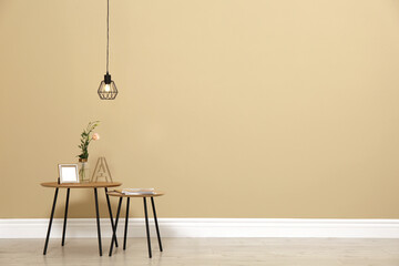 Small tables with decor near beige wall in room, space for text. Interior design