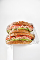 low view of two delicious tuna sandwiches with tomato and cucumber in paper on white box