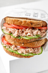 two delicious tuna sandwiches with tomato and cucumber in paper on white box