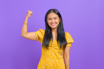Attractive young Asian woman showing muscle with smile expression on purple background