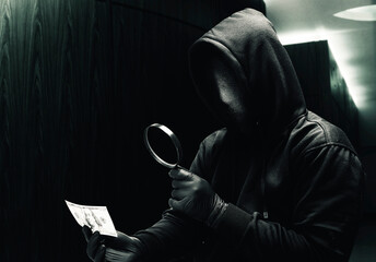 Criminal man in a hidden mask using magnifying glass while holding the money while robbery