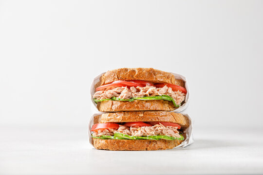 two delicious tuna sandwiches with tomato and cucumber in paper on light grey background