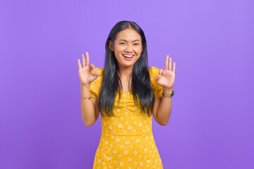 Cheerful young Asian woman makes okay gesture, demonstrates symbol of approval on purple background - obrazy, fototapety, plakaty