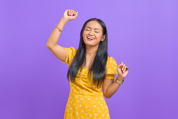 Portrait of excited young Asian woman celebrating success on purple background