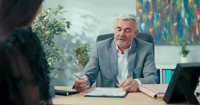 Job interview elderly boss with gray hair sitting at desk opposite him woman applying for secretarial position in company man asks girl questions discusses education salary expectations first contract