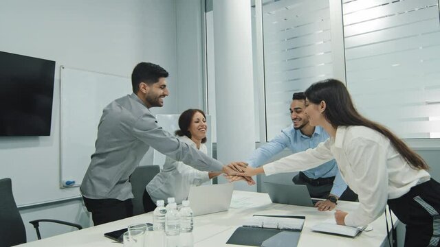 Excited multicultural cheerful businesspeople sitting together at meeting giving high five gesture multiethnic colleagues feels happy, showing team spirit, celebrating news victory goal achievement