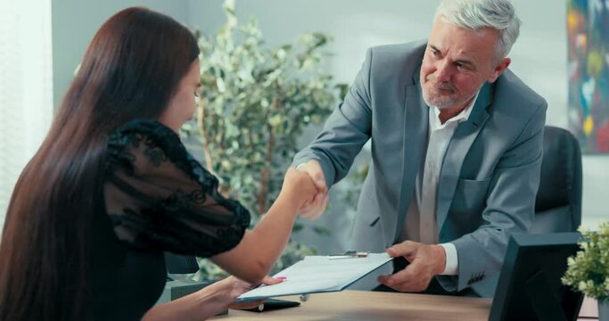 Mature boss of company signed contract with new employee, a candidate for position of assistant secretary in company man congratulates young woman holds contract and with other shakes hand of girl