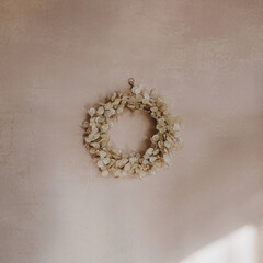 Gold Christmas wreath made of natural dry lunaria leaves hanging on a pink wall with sunlight shadows. New Year and winter holidays. Aesthetic Christmas decor