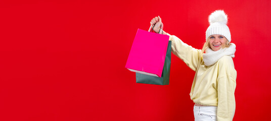 Banner holidays sales and shopping. Portrait of cheerful Woman in winter clothes with colorful shopping bags on red studio background. Mock up for logo. Addicted shopper want shop all bargains