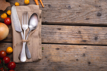 Food ingredients and multiple autumn leaves and cutlery set over a napkin on wooden surface