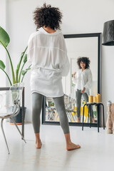 Young pretty mixed race woman with curly hair looking at herself in mirror. Checking out her outfit.