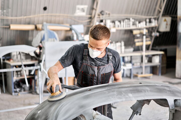The mechanic works with a grinding tool. Sanding of car elements. Painting car service. Repairing...