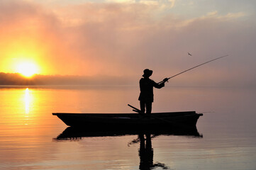 Lonely fisherman in the boat fishing on the misty river during sunrise