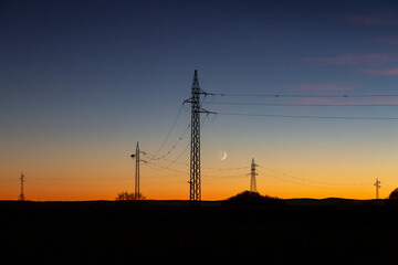 Power line and crescent moon at dusk in the El Páramo region, León, Spain.