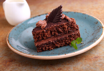 Piece of chocolate cake on a plate on a black background decorated with mint.
