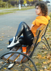 Obraz premium Young beautiful woman in orange knitting sweater holding cup with coffee in the autumn park.
