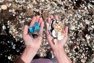 Man holds in one hand the waste collected on the seashore, in the other hand shells. Environmental pollution concept.