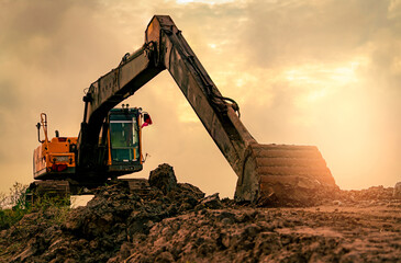 Backhoe parked at construction site after digging soil. Bulldozer on sunset sky and clouds background. Digger after work. Earth moving machine at construction site at dusk. Digger with dirt bucket.
