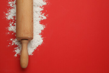 Wooden rolling pin and flour on red background, top view. Space for text