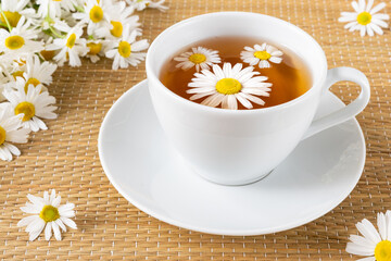 Healthy herbal tea in porcelain teacup with chamomile flowers on rattan matting