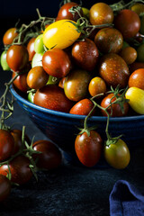 Naklejka na ściany i meble Fresh organic cherry tomatoes on a branch, colorful seasonal tomatoes in a bowl on a dark background
