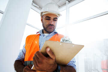 Foreman at work on construction site checking his notes on clipboard