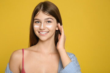Teenage girl with sun protection cream on her face against yellow background. Space for text