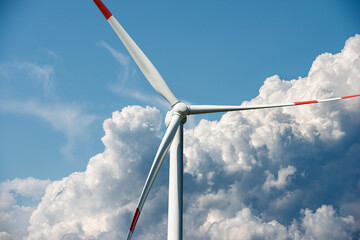 Red and white wind turbine against a blue sky with cumulus clouds and copy space. Renewable energy concept. © Alberto Masnovo