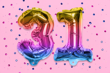 Rainbow foil balloon number, digit thirty one on a pink background with sequins. Birthday greeting card with inscription 31. Top view. Numerical digit. Celebration event, template.