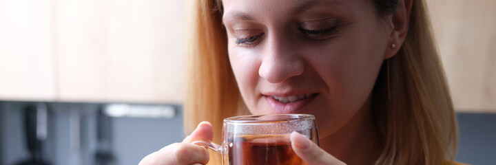 Young woman drinks tea from transparent cup closeup