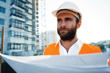 Builder or architect in hardhat supervising a project, looking at blueprints