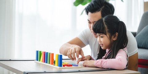 Cheerful and playful cute little girl learning numbers and math with handsome young father at father by playing with blocks for educational development at home