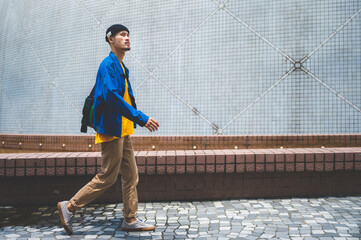 Young male hipster in casual clothing walking down the footpath while looking away