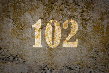 Number one hundred two. White enumeration on the old concrete surface. The number 102 written with overlapping tones. Early retirement concept.