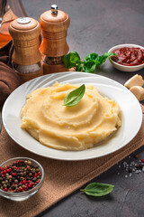 Mashed potatoes in a white plate on a background of spices, sauce and basil.