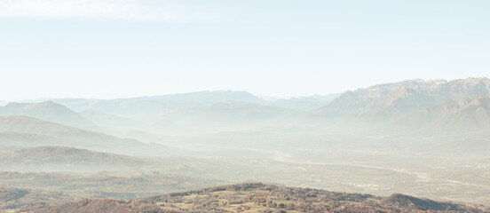 Winter landscape of the Italian mountains. View of the Belluno Dolomites from Nevegal. Mountains with light haze illuminated by the sun. Climate change concept.	Artistic horizontal image. 
