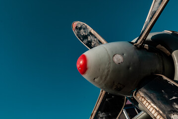 an old peeling, broken propeller from an airplane with a red spot of paint on the edge against a bright blue sky