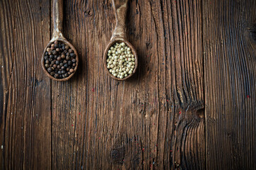 Black and white pepper on an ceramic spoon over wooden backround