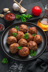 Meat Meatballs with fresh basil close-up in a black plate on a dark background.