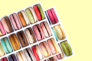 Multicolored macarons or macaroons with varied flavors in box isolated on yellow background. Top view, close-up