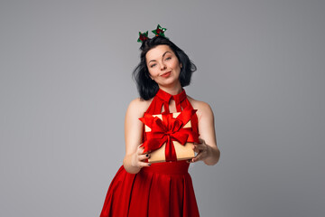 Happy young brunette woman in red dress posing on gray background with gift box decorated with red ribbon. Holidays, celebration and lifestyle concept