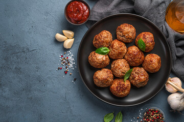 Fried meatballs with basil on a dark background with tomato sauce and garlic.