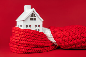 White toy house wrapped in red scarf on red background. Heating or insulating buildings or houses...