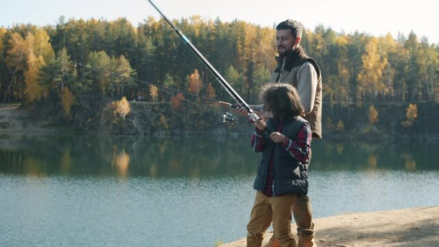 Young father and little son are catching fish in river using fishing rods on autumn day. Family lifestyle and relationship concept.