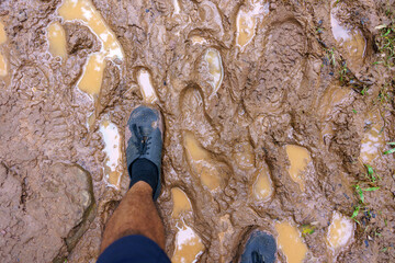 View from above on pair of trekking shoes in a mud, Hiking boots stuck in mud