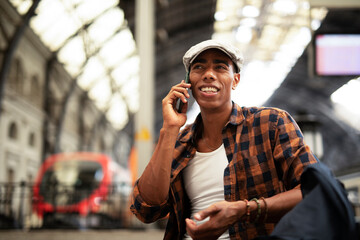 Happy young man waiting for the train. African man waiting in a subway. Man using a phone..