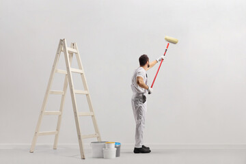 Ladder and buckets in a room and decorator painting a wall
