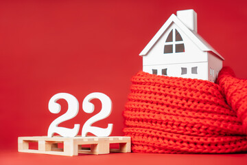 Happy New Year 2022. White numbers 22 on pallet with white toy house wrapped in red scarf. Merry...