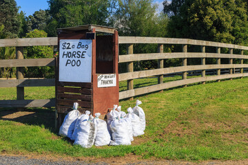 Bags of horse manure for sale from a small stall just outside a farm. Photographed in New Zealand
